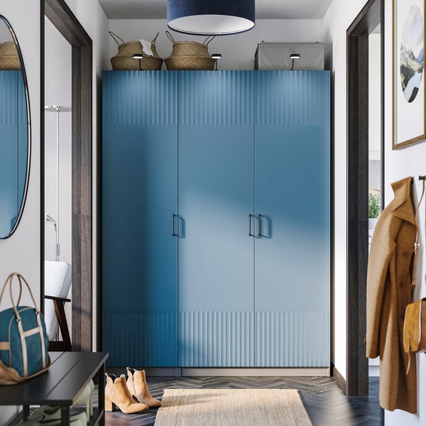 Moderní vstupní hala s vysokou modrou šatní skříní PAX, elegantním designem, obklopená kulatým zrcadlem, věšáky na kabáty a malou lavicí.