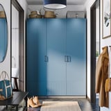 Moderní vstupní hala s vysokou modrou šatní skříní PAX, elegantním designem, obklopená kulatým zrcadlem, věšáky na kabáty a malou lavicí.