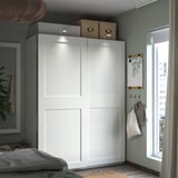Moderní ložnice s bílou šatní skříní PAX, posuvnými dveřmi, integrovaným osvětlením a úložnými boxy.
