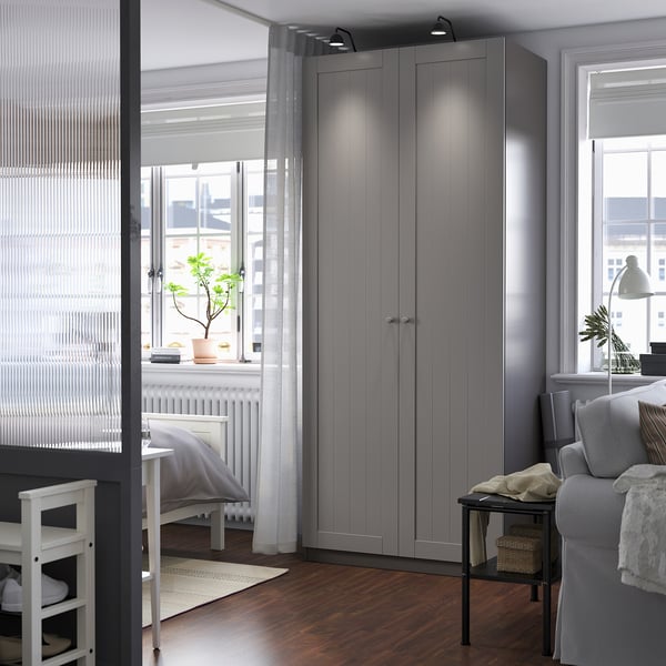 Moderní šedá šatní skříň PAX v útulném pokoji. Vysoký, elegantní se svislými drážkami. V blízkosti pohovka, stůl, bílý radiátor.