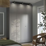 Moderní ložnice vysoká šedá šatní skříň PAX s elegantním designem, sladěným proutěným křeslem a zelenou přikrývkou na posteli.