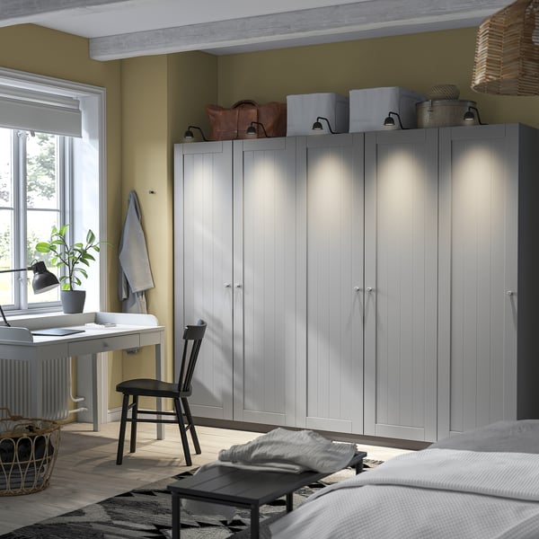 Velký pokoj s vysokými bílými skříněmi PAX. Psací stůl se židlí a okny. Moderní, minimalistický design.