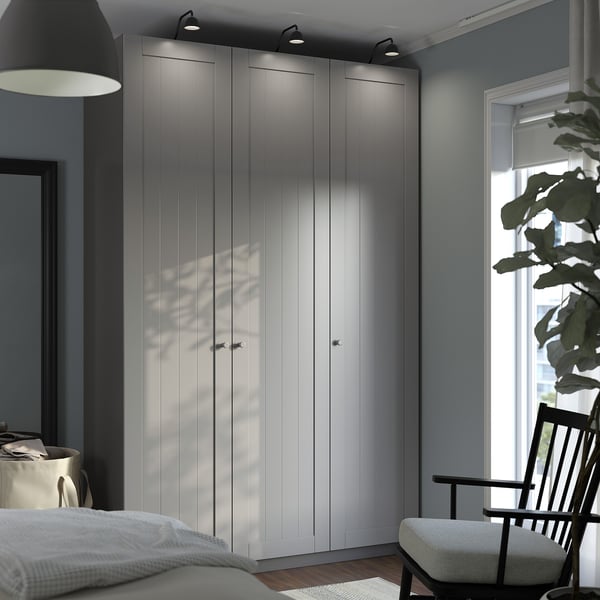 Velká šedá šatní skříň PAX s elegantním, jednoduchým designem se tyčí vysoko u okna a pojme prostor s moderním dekorem.