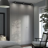 Velká šedá šatní skříň PAX s elegantním, jednoduchým designem se tyčí vysoko u okna a pojme prostor s moderním dekorem.