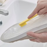 Osoba používající malý žlutý štěteček k vyčištění skvrn z bílé tenisky.