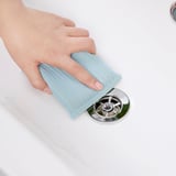 Osoba čistí chromovaný odtok dřezu modrou pračkou PEPPRIG.