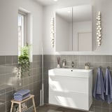 Moderní koupelna s bílým umyvadlem, zrcadlem, šedými dlaždicemi, modrými ručníky, rostlinou a mopem.
