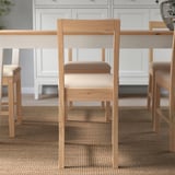 Minimalistická dřevěná židle s čalouněným sedákem u stolu, která vyniká svým pohodlným designem pro dlouhé sezení.