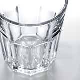Vysoce kvalitní, průhledný skleněný pohár s geometrickým designem, odrážející světlo, stojí na lesklém povrchu.