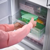 Osoba otevírající ledničku pro přístup k plastovým nádobám na skladování potravin různých velikostí, které se používají k ukládání zbytků a šetří místo během skladování.