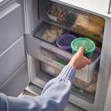 Osoba popadající zelenou nádobu z lednice, ukládající zbytky nebo svačiny, ideální pro školní nebo pracovní obědy.