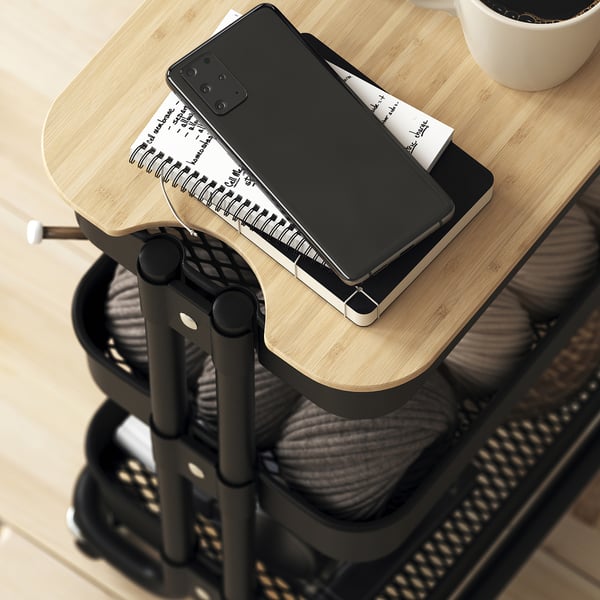 Malý černý mobilní vozík s dřevěnou horní částí pojme smartphone, notebook a hrnek a poskytuje všestranné úložiště a pracovní prostor.
