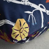 Detailní záběr zářivého, detailního povlaku na polštář se žlutou květinou a botanickým vzorem na tmavě modré látce.