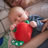 Dítě leží na gauči a drží v ruce hračku jablko SANDBI s červem; Hračka vydává uklidňující zvuky.