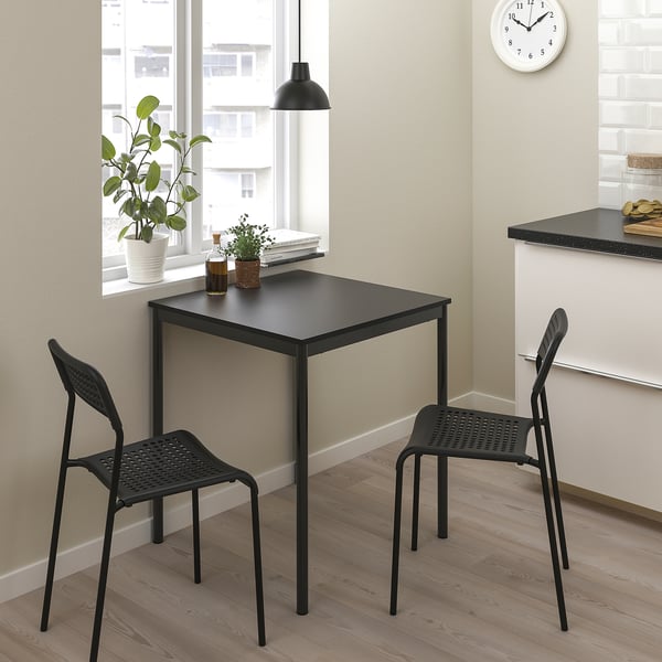 Malý černý sandbergový stůl a židle v rohu u okna. Moderní, prostorově úsporný design s kovovými rámy. Ideální pro malé místnosti.