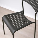 Černá perforovaná židle s elegantními kovovými nohami na dřevěné podlaze.