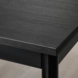 Detailní záběr na moderní černý stůl s hladkým, elegantním povrchem a robustními kovovými nohami, který ukazuje jeho vysoce kvalitní design.