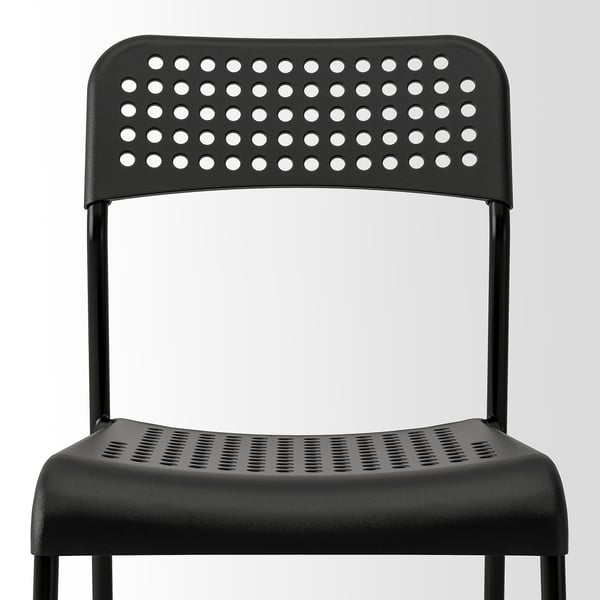 Černá židle s perforovaným sedákem a opěradlem, pevná kovová kostra, stohovatelný design.