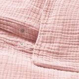 Světle růžové, měkké povlečení z organické bavlny s kovovými uzávěry, zobrazené v úhledně uspořádané hromádce.