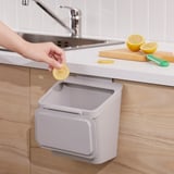 Osoba vyhazující citronovou kůru do nástěnného odpadkového koše pod kuchyňským dřezem.