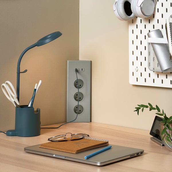 Modrý prodlužovací kabel na dřevěném stole s lampou, notebookem a rostlinou. Minimalistický design.