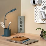 Modrý prodlužovací kabel na dřevěném stole s lampou, notebookem a rostlinou. Minimalistický design.