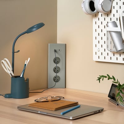 Modrý prodlužovací kabel na dřevěném stole s lampou, notebookem a rostlinou. Minimalistický design.