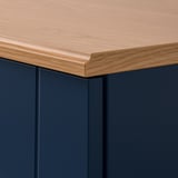 Detail hrany skříně SKRUVBY s hladkým, dubovým povrchem a tmavě modrými boky.