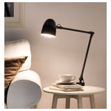 Lampa SKURUP na stole vedle bílé židle, moderní design.