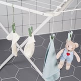 Kolíčky na prádlo věší oblečení na sušák, včetně dětských předmětů a plyšového medvídka.