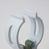 Dva bílé kolíčky na prádlo, jeden zelený, robustní a připravený na těžké prádlo, na světle šedém pozadí.