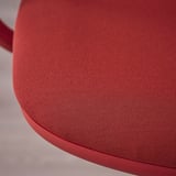 Detail červené látky kancelářské židle. Hladký, texturovaný povrch naznačuje vysoce kvalitní, odolný materiál, navržený pro pohodlí a dlouhou životnost.