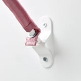 Dětská ruka se natáhne k bezpečně namontovanému bílému nástěnnému držáku, který demonstruje robustní design a bezpečnost v minimalistickém prostředí.