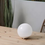 Solární lampa SOLVINDEN na dřevěném stole s rostlinou.