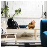 Moderní konferenční stolek s elegantním a lehkým designem. Masivní borovicové dřevo dodává teplo. Umístěný u bílé cihlové zdi, držící dekorativní předměty.