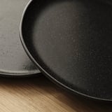 Tmavě skvrnité matné talíře naskládané na dřevěném povrchu, předvádějící jemné řemeslné zpracování a rustikální eleganci.
