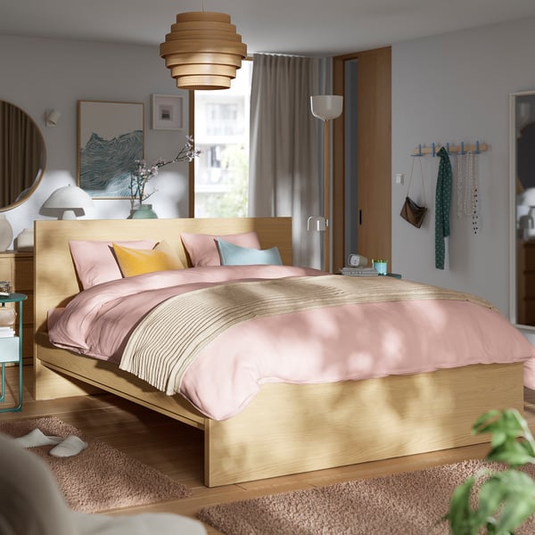 Moderní ložnice s postelí STORKLINTA, růžovým povlečením, minimalistickým dekorem a velkým oknem.