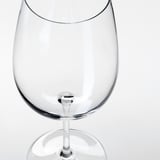 Čirá, prázdná sklenice na víno s hladkým stonkem, odrážející světlo, na bílém pozadí.