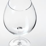 Čirá, prázdná sklenice na víno s dlouhou stopkou a širokou mísou, odrážející světlo, na bílém pozadí.