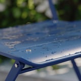 Modré kovové sedák židle s kapkami vody; moderní, outdoorový design.