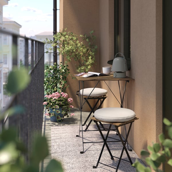 Malý balkon se dvěma bílými stoličkami TÄRNÖ a kovovým odkládacím stolkem s šedou konvicí a růžovými květinami v květináčích.