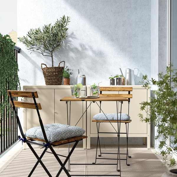 Kompaktní balkon se stolem a židlí TÄRNÖ, rostlinami a šedým polštářem.