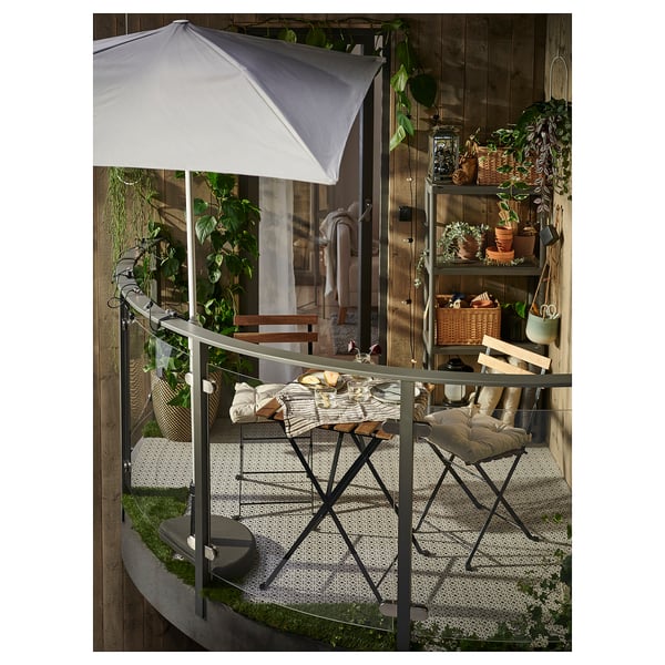 Útulný balkon se stolem a židlemi TÄRNÖ, bílým deštníkem, bujnými rostlinami a rustikální výzdobou.
