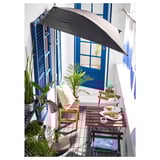Malý balkon s dřevěným nábytkem TÄRNÖ, modrými akcenty, rostlinami a stínícím deštníkem.