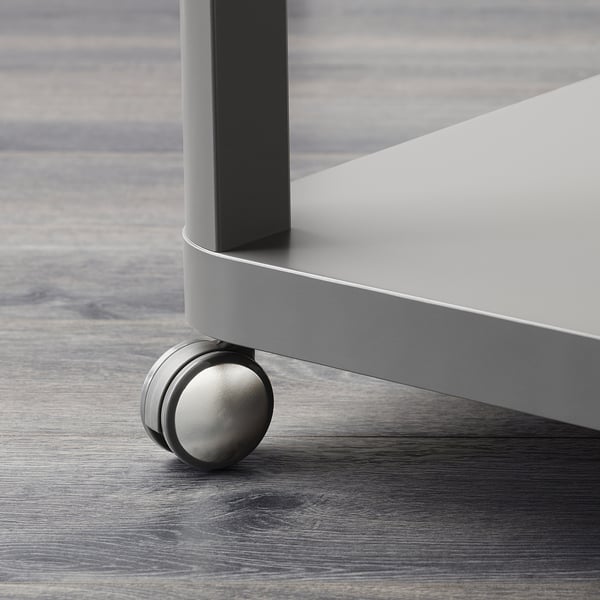 Detail moderní kovové nohy stolu s hladkým kolečkem na dřevěné podlaze.