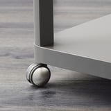 Detail moderní kovové nohy stolu s hladkým kolečkem na dřevěné podlaze.