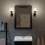 Moderní koupelna se zrcadlem TOFTBYN, nástěnnými lampami, umyvadlem, zubními kartáčky a toaletními potřebami.