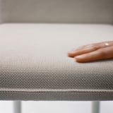 Detailní záběr na měkkou, tkanou, šedou desku stolu pod jemnou rukou zobrazující kvalitní texturu a řemeslné zpracování.