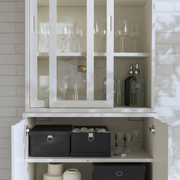 Elegantní bílá skříň TONSTAD se skleněnými dvířky a šedými boxy, na které se ukládají sklenice na víno a ozdobné lahve.