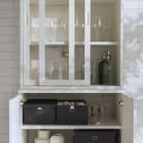 Elegantní bílá skříň TONSTAD se skleněnými dvířky a šedými boxy, na které se ukládají sklenice na víno a ozdobné lahve.